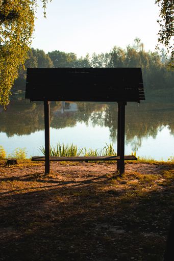 A vertical shot of a wooden bench with a roof on the shore of the lake in the park in autumn