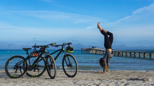 A young woman practicing sports on the seashore with two bicycles on the side
