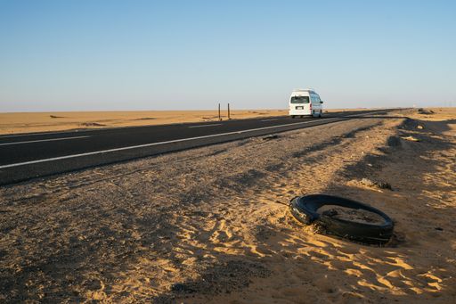 A white car driving on the asphalt road through sandy deserts