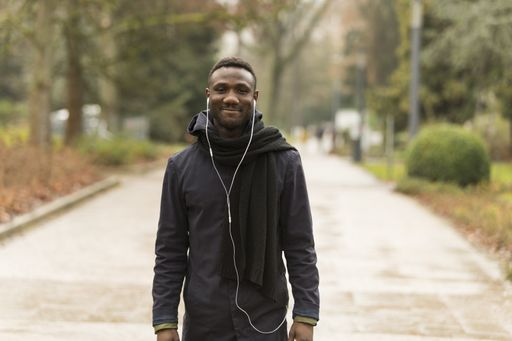 A selective focus shot of a smiling black male with earphones walking in the streets