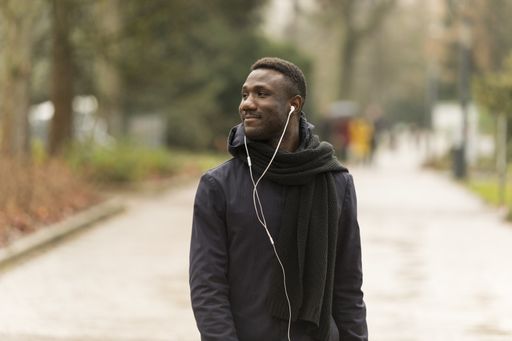 A selective focus shot of a smiling black male with earphones walking in the streets
