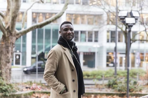 A selective focus shot of a smiling black male with earphones walking in the streets