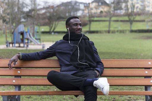 A selective focus shot of a smiling black male with earphones sitting in the park