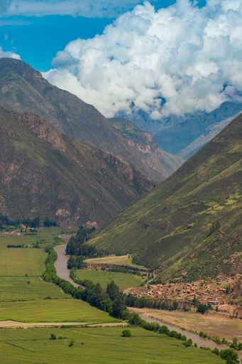 An aerial beautiful landscape view of highway between green grass fields and high mountains