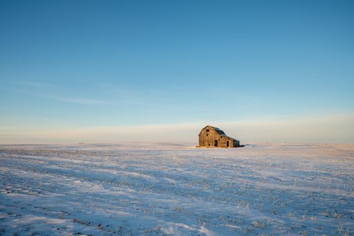 Old barn in a rural field with wind turbines in the distance.
