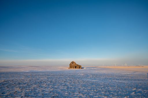 Old barn in a rural field with wind turbines in the distance.