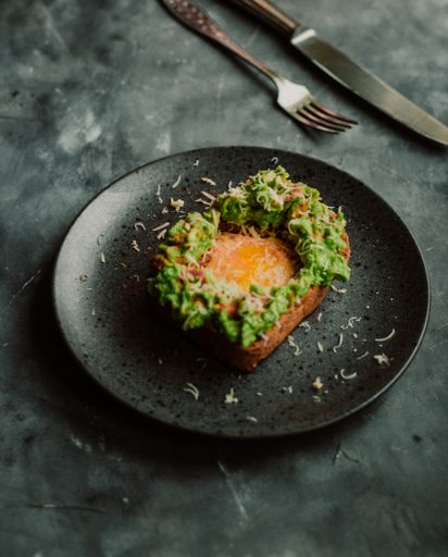 A vertical selective closeup shot of a fried bread with eggs and avocado on a black plate