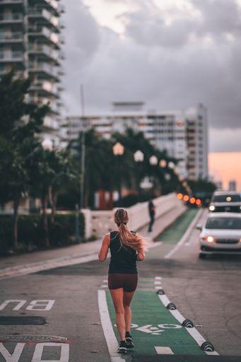 A vertical back view of a female running on a sidewalk in the evening