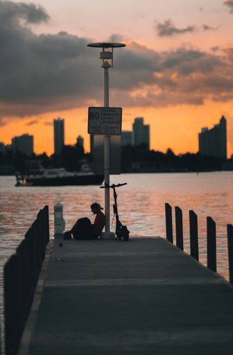 A silhouette of a person sitting near a bike on the bridge over the sea on a golden sunset background