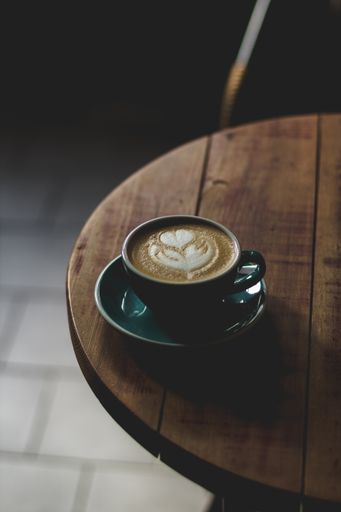 A vertical selective closeup shot of coffee with latte art in a blue ceramic cup on a wooden table