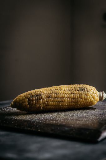 A vertical selective closeup shot of corn on a brown wooden chopping board