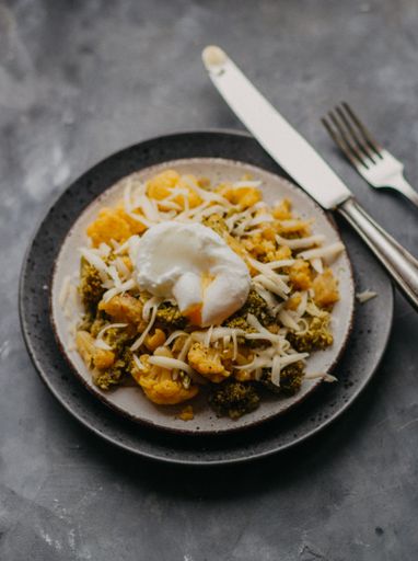 A vertical selective closeup shot of a dish with broccoli, cauliflower and egg on a gray plate