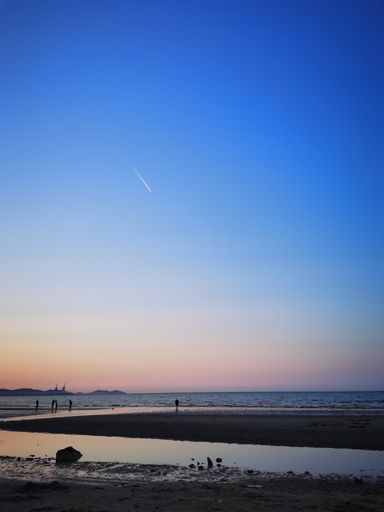 A vertical shot of the wavy sea with a sandy beach and people on the shore in sunset