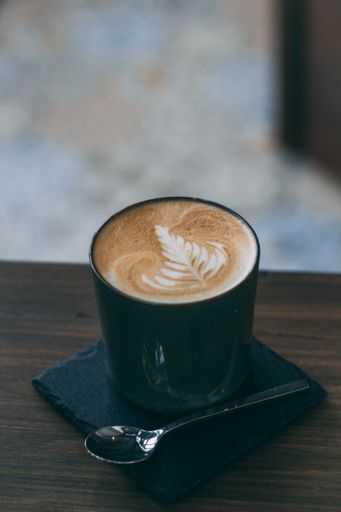 A vertical selective closeup shot of coffee with latte art in a blue ceramic cup and teaspoon on a wooden table