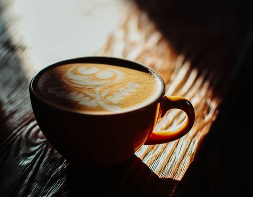 A vertical selective closeup shot of coffee with latte art in a red ceramic cup on a wooden table
