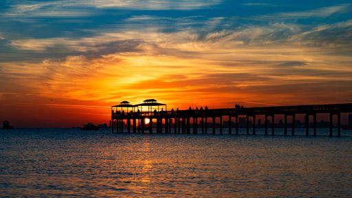 A wooden pier in calm water with a quiet but cloudy sky in the background in a beautiful evening
