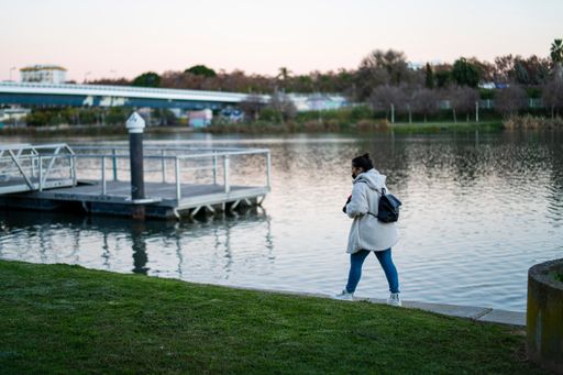 A girl with a small backpack and a warm coat walking on the riverside on a cold autumn day in the park