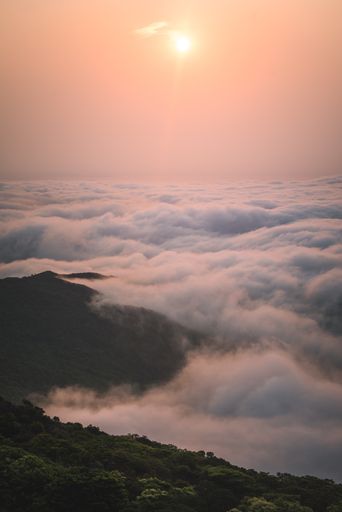 A vertical shot of the clouds covering the mountains at sunset