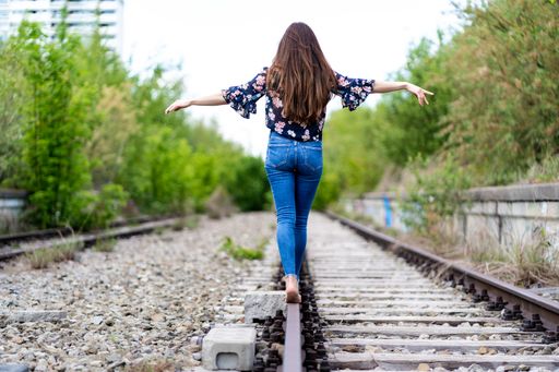 The back of a young female walking through the train rails barefoot and trying to hold the balance