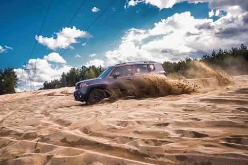 The gray Jeep driving over the sandy dunes on a sunny day.