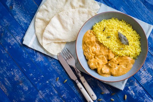 A top view of cooked Indian food chicken korma with pilau rice and cardamom seeds on a wooden table