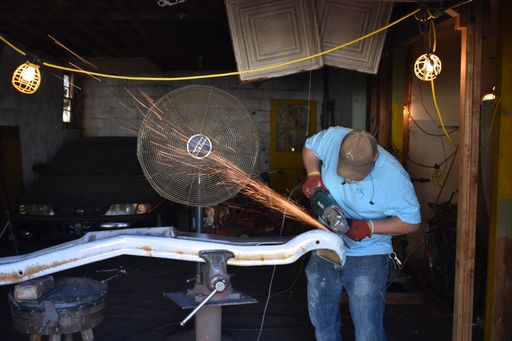 A man grinding a car bumper in a workshop, creating sparks