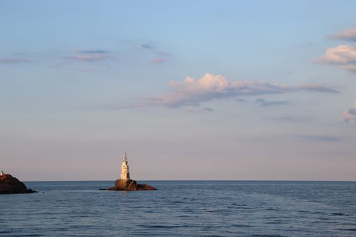 A scenic view of a lighthouse in the middle of an ocean on cloudy sky background