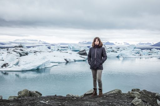 A young female standing on a rocky ledge enjoying the view of the glacier in Jokulsarlon, Iceland