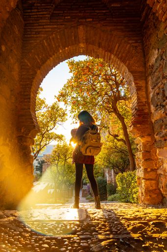 A vertical shot of a tourist at sunset at the gate of the Alcazaba wall in the city of Malaga
