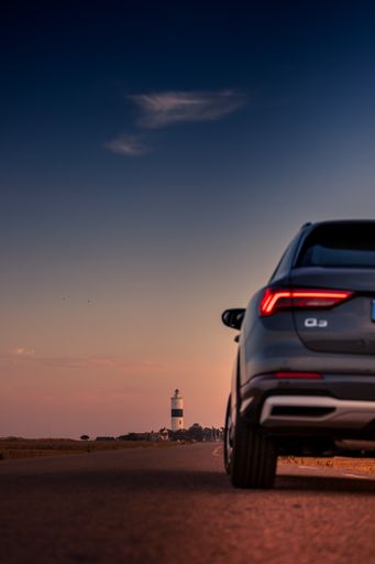 A vertical shot of a gray Audi Q3 car on a trip to a lighthouse at sunset