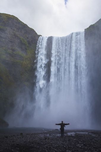 A vertical shot of a male with open arms near Skogafoss waterfall in Iceland