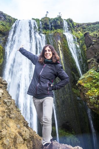 A vertical shot of a happy woman near the Seljalandsfoss waterfall in Iceland