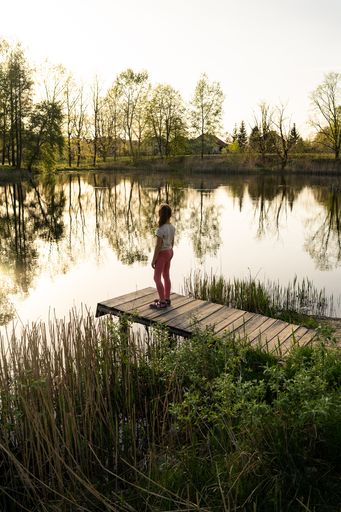 A vertical shot of a young woman at the pier bridge by the lake during sunset