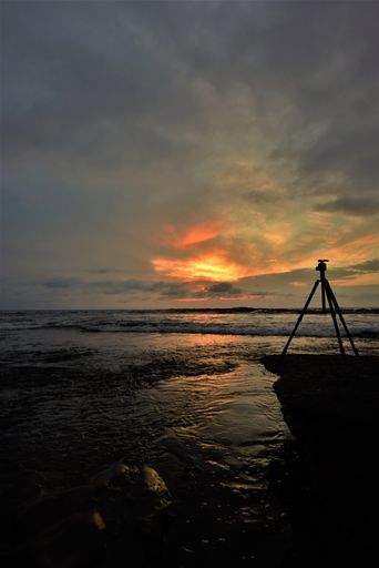 A silhouette shot of tripod with camera on a rock during sunset