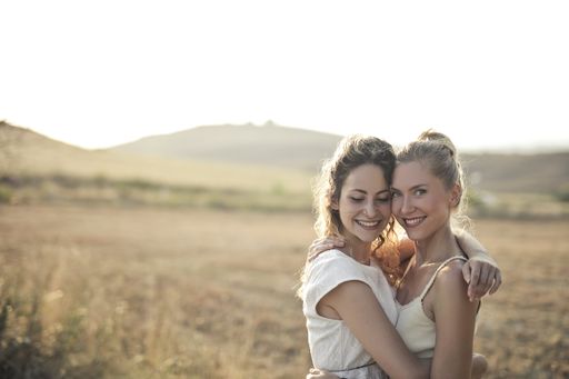 Two young women smiling and hugging each other in the field