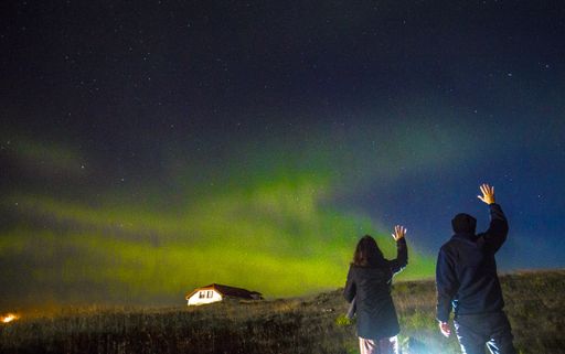 A couple of young man and woman looking Northern lights on the Reykjanes Skaginn Peninsula in Iceland