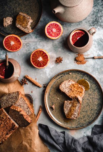 A vertical high angle shot of a grey table with bread, spices, grapefruit, tea, and kettle on it