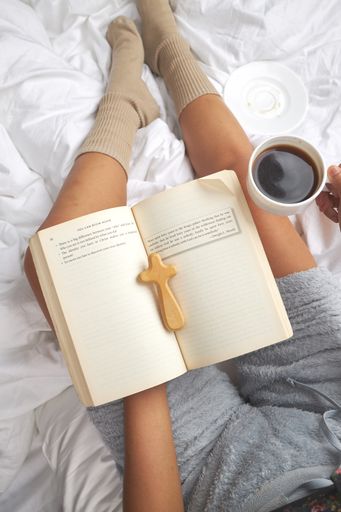A vertical shot of reading the bible and drinking coffee in the bed