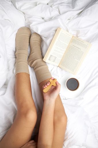 A vertical shot of a female in the bed holding a wooden cross, with the bible and a cup of coffee