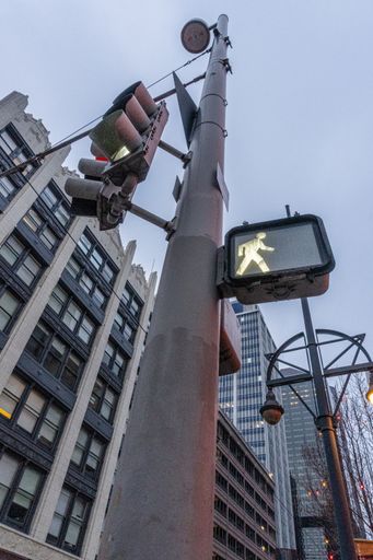 A vertical shot of a pedestrian crossing sign on a tall pole in the city