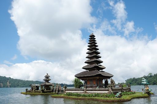 The Ulun Danu Beratan Temple surrounded by water and greenery under a blue cloudy sky in Bali, Indonesia