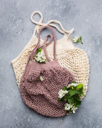 A vertical closeup shot of white flowers with green leaves on a beige and pink knitted bags