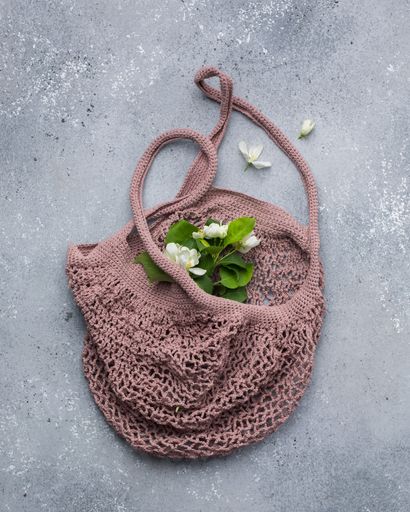 A vertical closeup shot of white flowers with green leaves on a dark dusty pink knitted bag