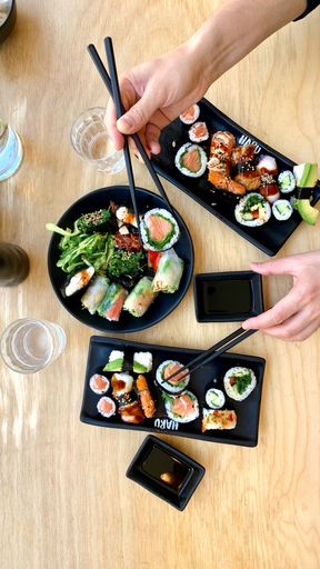 A vertical overhead shot of variety of sushi rolls on white plates on a wooden table