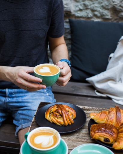A vertical selective closeup shot of a person holding a cup of latte art coffee near a table with pastries on plates