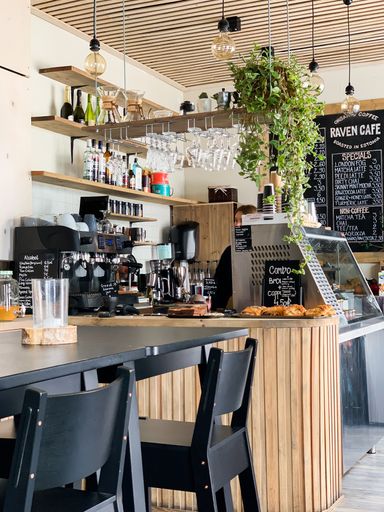 A vertical shot of a black wooden table with chairs,coffee machines, glasses and bottles in a coffee shop