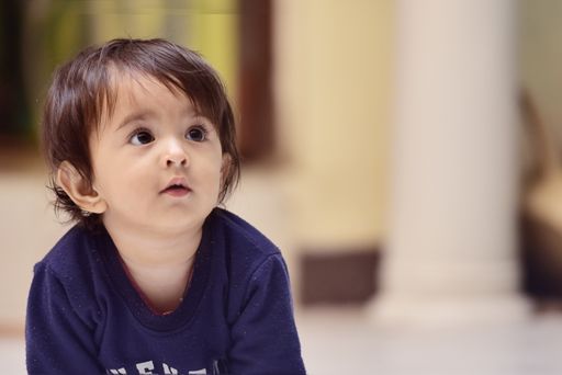 A close-up shot of a cute South Asian baby boy sitting and looking with a curious face