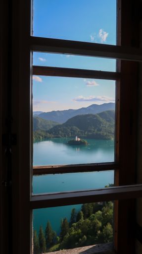 A vertical shot of the Lake Bled and mountain landscape is seen through a window