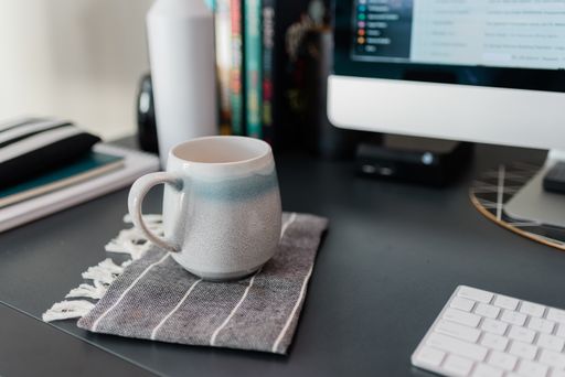 A selective focus shot of a white cup on a desk near a computer at an office
