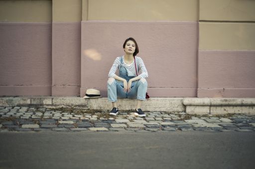 An attractive young female sitting on the sidewalk under the sunlight at daytime